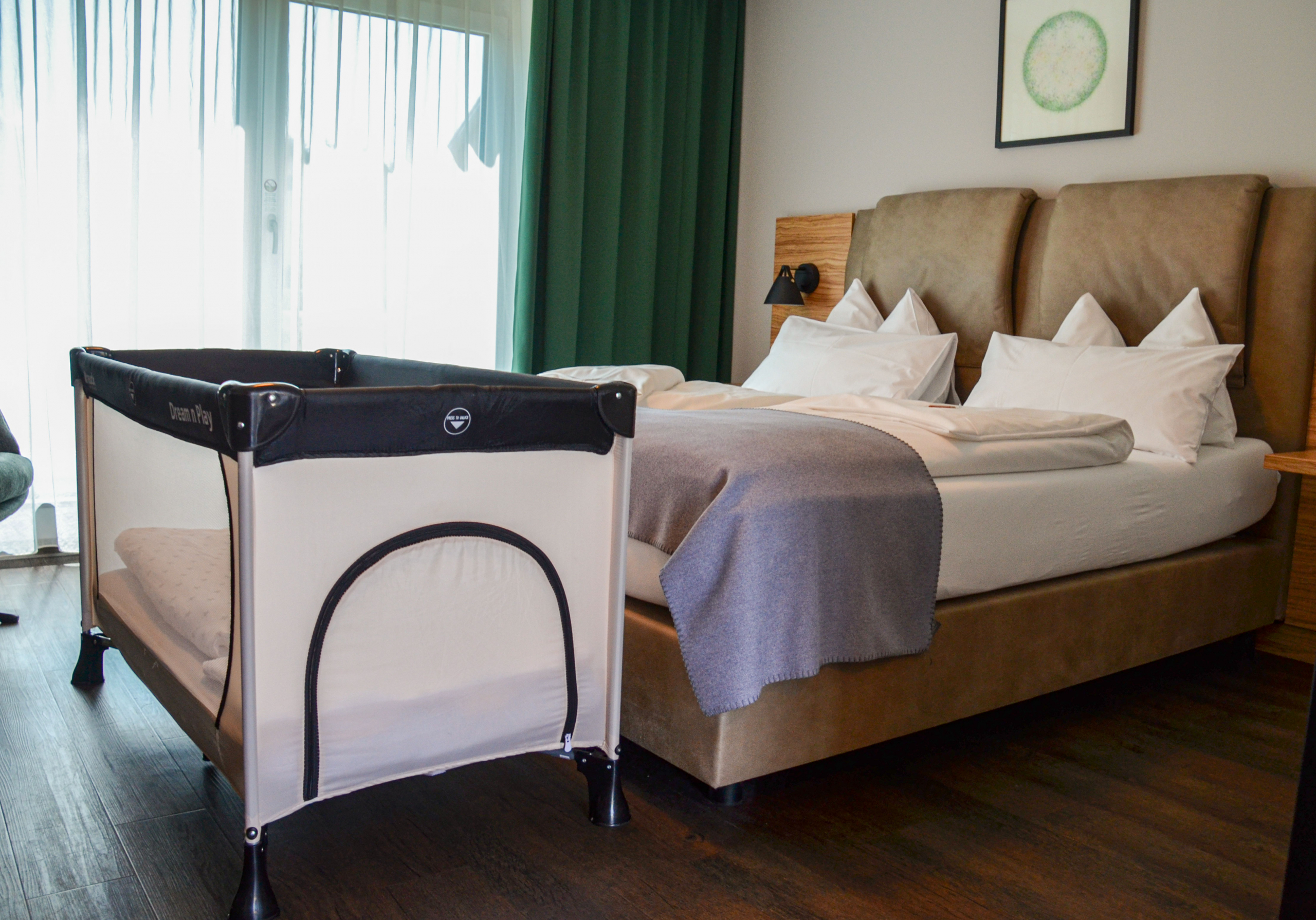 Ein Babybett steht vor dem Doppelbett im trendic hotel Zimmer.