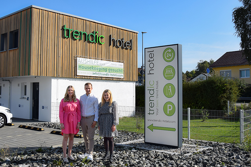 Zu sehen sind die beiden Geschäftsführerinnen Nina und Jana Höbel und der Hotelmanagaer Johannes Seyfried-Höbel vor dem trendic hotel stehend.